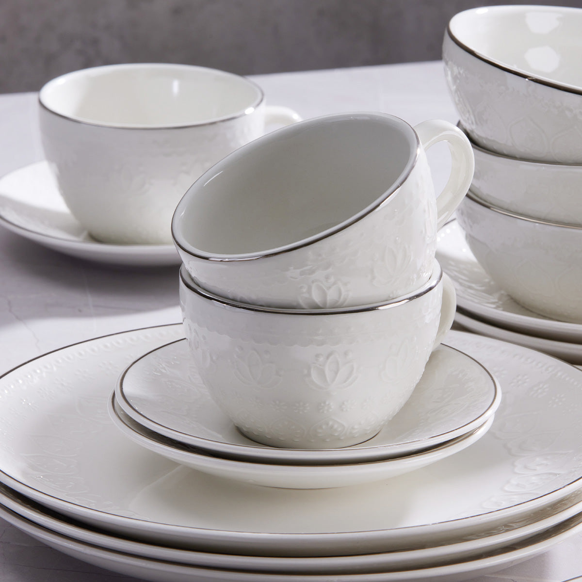 Vajilla Harmony Corona 20 piezas: tazas, platillos, bolos y platos en loza de alta calidad con relieve floral y filo plateados.
